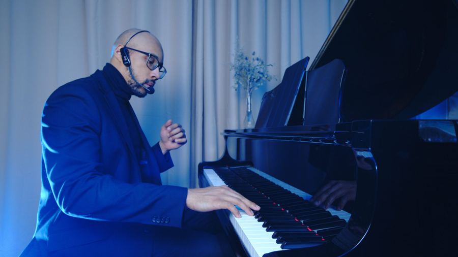 Jeremy Ajani Jordan playing a grand piano under blue stage light, side profile view